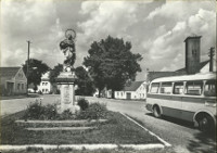 Na pohlednici je nves s tvercovm trvnkem lemovanm kamennm
            obrubnkem. Na trvnku je na baroknm kamennm podstavci socha Panny
            Marie, dobov autobus (tehdy se zaoblenmi hranami -aerodynamitj
            proveden), za autobusem je vidt hasisk zbrojnice (hasirna) s
            devnou v na suen hadic.