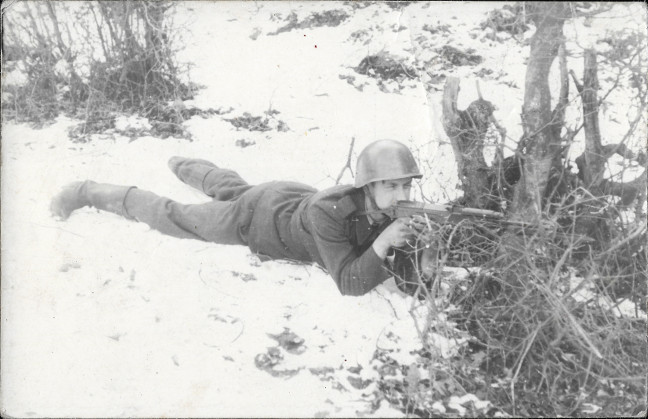 Na fotografii velkho formtu je zachycen vojn v khaki poln uniform lec pipraven ke stelb na snhu za keem.