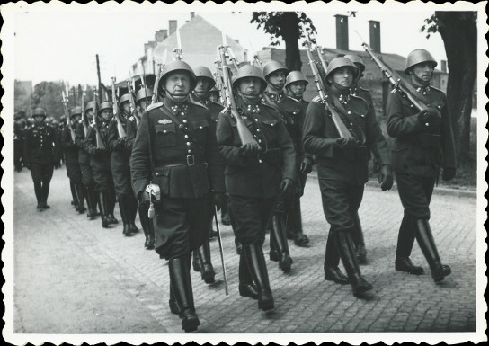 Na fotografii je zachycen pochodujc tvar. Na hlavch
          maj vojci eskoslovenskou plbu vz. 1932 a zen kalhoty zasunut do
          holnek. Ti vpedu maj jezdeck. Je vidt i opasek se dvma trny a rmovou
          pezkou.