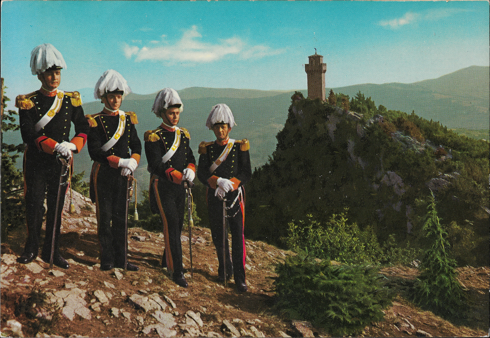 Vrazn spoleensk uniforma zahrnuje tmav modr kalhoty a dvouad frak, se zlatmi ozdobami, vetn dvojitho pruhu na nohavicch, nramenk, manet, lmc a zadnch okraj
  fraku. Tmav modr kalhoty maj dvojit zlat lampas pro dstojnky a v ziv luto-zlat ltce pro ostatn hodnosti. Soust tto uniformy jsou tak bl rukavice, bl koen
  emen od levho ramene k pravmu boku. Dvouroh klobouk maj zdoben modrmi a blmi pery. Pro ceremoniln povinnosti tato sla nos avle. Na ramenou m tmav modr epolety se
  zlatm lemem, zlatou aplikac a tsnmi. Zlat ozdoba je tak na emenu pes rameno. Lmce maj erven. Zahrocen dvakrt vykrojen manety v barv lampas a hodnostn oznaen
  maj v podob irokch ervench krokvic sledujcch v mal vzdlenosti okraje manet. Na pohlednici nen na kloboucch vidt modr pera. Skupina ty gardist stoj na kamenitm
  svahu s dkm porostem. Pes dol je vidt skalnat vrchol s v pevnosti a v dlce poho.