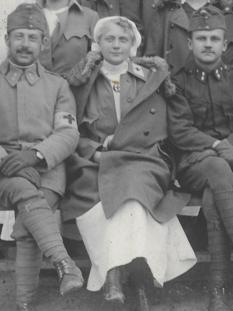 Lkai na detailu fotografie maj ern prouky s dvma hvzdikami na lmcch. Lmce maj leat, take je fotografie z roku 1916 nebo pozdjho data. Sestra
  m pl᚝ i blzu rozepnutou. Je tedy vidt bl tek, bl pl᚝, pod krkem kruhov sestersk odznak s ervenm kem uprosted, jednoadovou blzu s ervenm kem
  na bl vloce a dvouad pl᚝ s koeinovm lmcem. Sestry maj vysok nrovac boty.