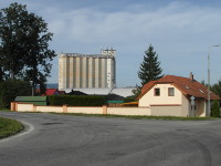 Na zbru fotografie z vletu je trochu v pozad za domem se zahradou a za plechovou halou silo dostavn roku 1975. 
          Fotografie je pozena pes kiovatku. Vlevo je listnat strom a za domem smrk.