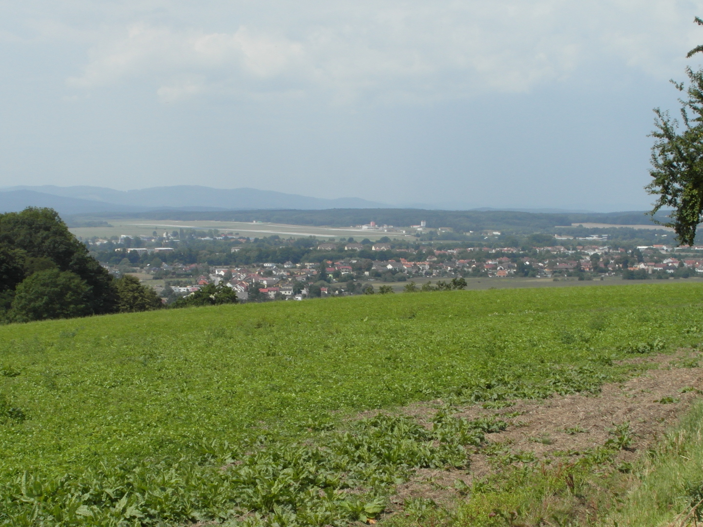 Na fotografii z vletu zabr prakticky celou spodn polovinu pole. Pak jsou vidt budovy,
  pistvac drhy letit, v dlce, za nimi les a na obzoru edomodr poho Blanskho lesa.