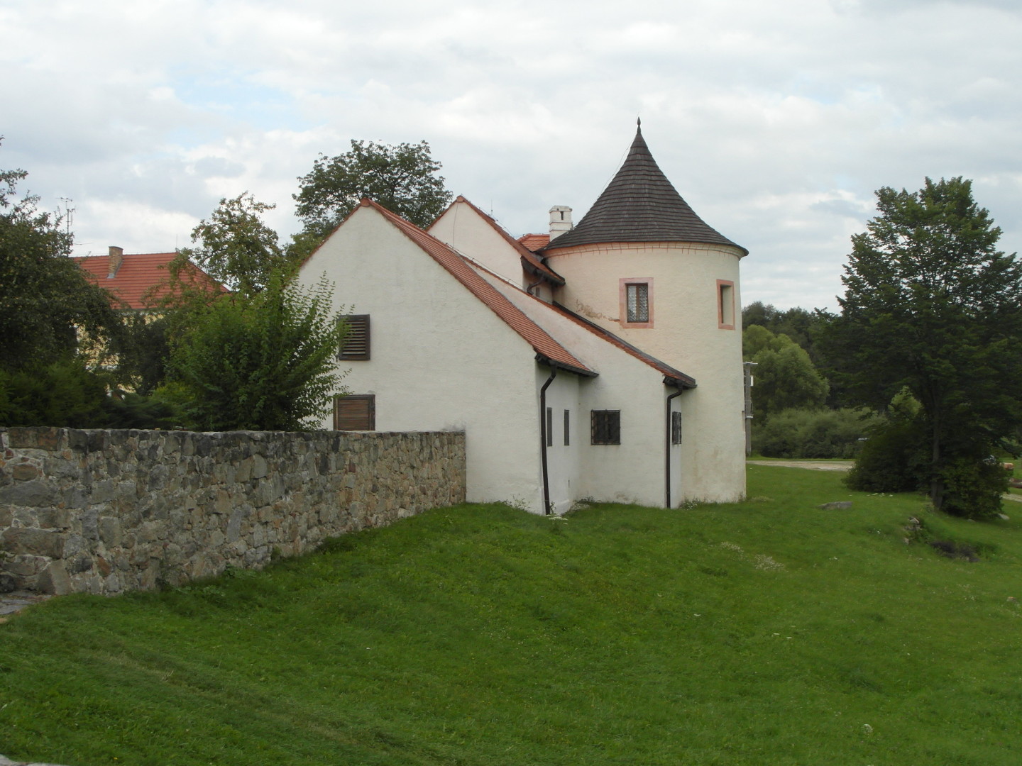 Na zbru fotografie z vletu je neomtnut hradba a dva ble omtnut domky pistavn k ble omtnut bat. Bata m rov doplky. Ped hradbou a batou 
  je trvnk a vzadu cesta, strom a les. Za hradbou jsou stromy. V pozad za hradbou vynv velk lut budova a za domy velk strom.