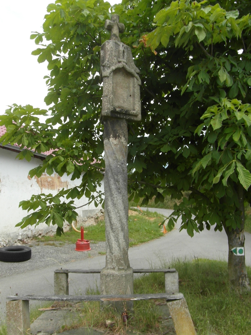 Na fotografii z vletu jsou kamenn sloupov Bo muka s ohrdkou, silnice a budova. 
  Hlavice Boch muk je ozdobn a je umstna na korintskm sloupu. Na hlavici je kamenn
  kek.