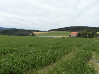 Na fotografii jsou vidt louky, kopce, pole, lesy a domek.