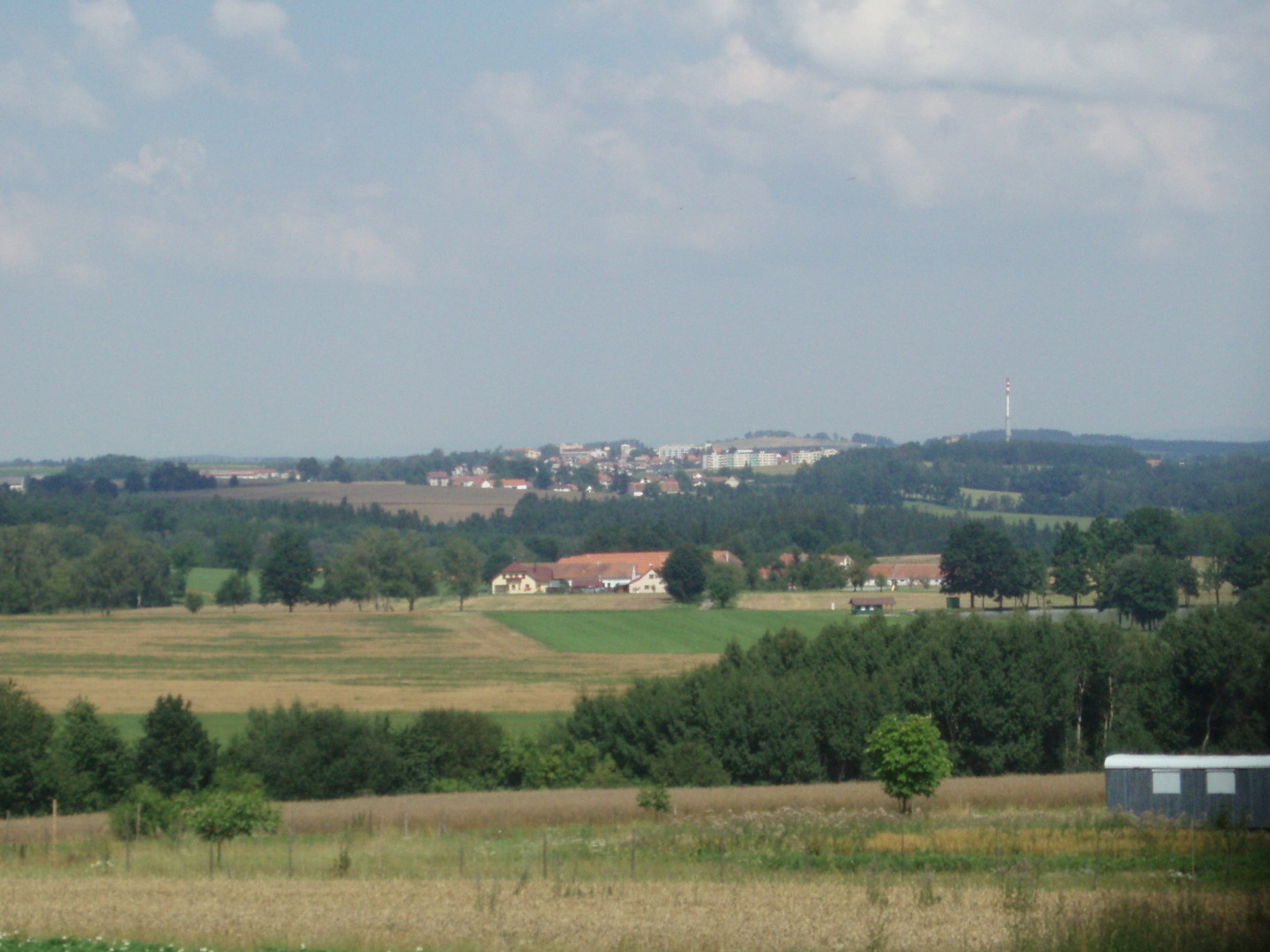 Na fotografii jsou louky, pole, lesy, stromy, maringotka a v dlce domky, 
  rybnk se zelenou chatkou a pln na obzoru msto Velen.