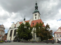 Na fotografii je v a lo kostela. Kostel je bl. Na vi jsou bn pokryt mdnkou. st lodi kostela zakrvaj
          stromy. Napravo je st domu. Dm m bledou rovou barvu s ervenou vzdobou.