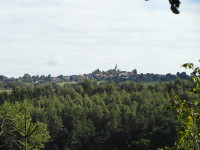 Na fotografii je les, nad lesem trochu louky a pole a vesnice s kostelem.