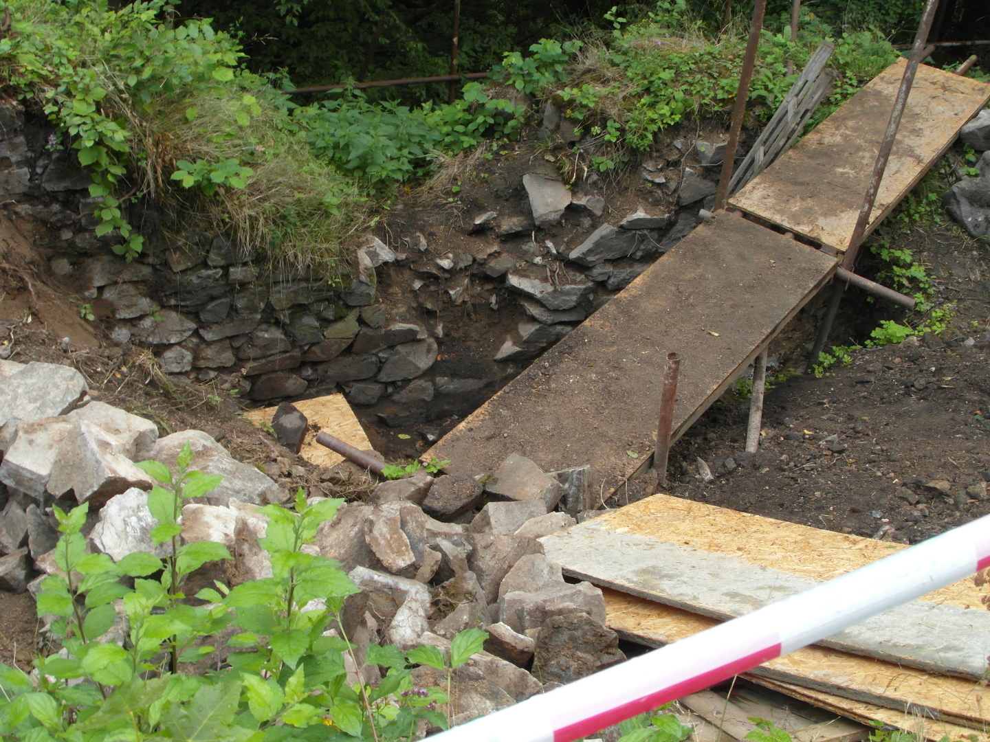 Na fotografii z vletu jsou prkna a ocelov leensk trubky v archeologick sond. V hlubokm vkopu je vidt odhalen ze, kameny, porost. 
  Nechyb ani bezpenostn ervenobl pska.